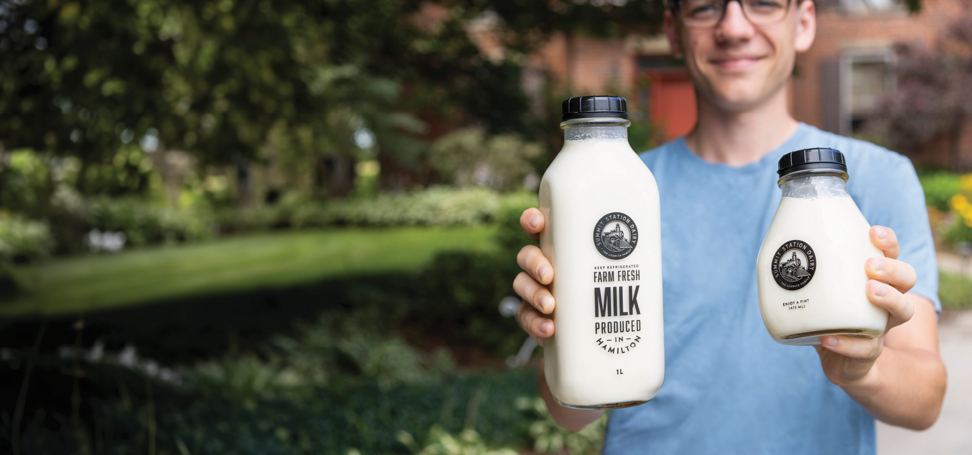 Teenage boy in light blue shirt holding up a 1L and 473ml bottle of whole milk in front of the camera